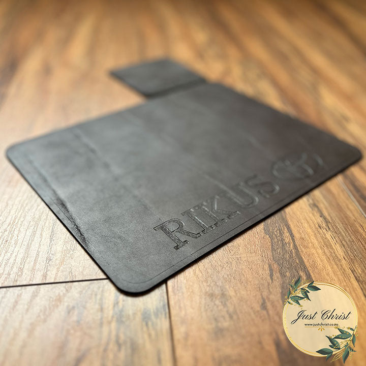 A dark brown standard mousepad is on wood laminated flooring. The image is taken from an angle. There is engraving on the mousepad with a Toyota logo and the name "Rikus."