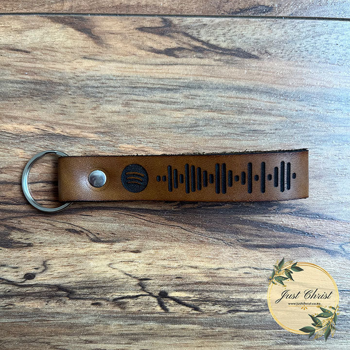 A Spotify code keyring is placed on a wooden background. 