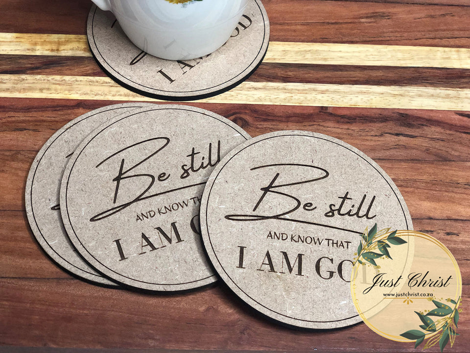 A set of four MDF coasters, strategically placed to slide from each other and placed on a wooden background. "Be still AND KNOW THAT I AM GOD" is engraved on the circle coasters.