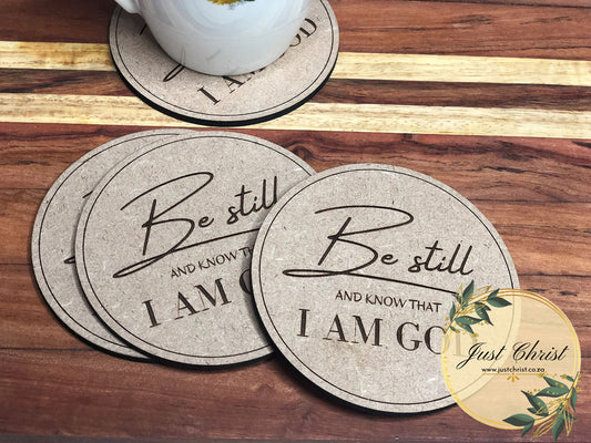 A set of four MDF coasters, strategically placed to slide from each other and placed on a wooden background. "Be still AND KNOW THAT I AM GOD" is engraved on the circle coasters.