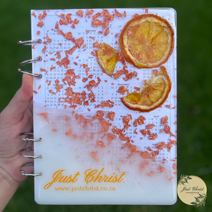 A resin notebook is held, there is dried oranges, copper flakes and vinyl used in the resin cover.