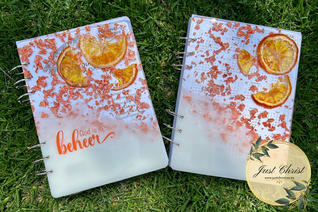 Two similar notebooks with resin covers are placed on grass.