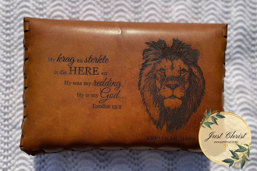 The backside is shown of a beige leather bible cover. The verse "Exodus 15:2" is engraved on the left side and a lion head (cat) is engraved on the right side.