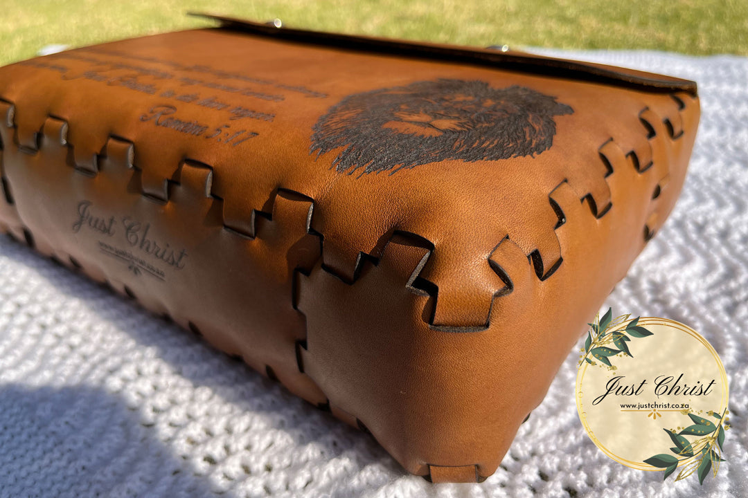 A photo o a leather bible cover placed on a blanket and taken from an angle. The photo boasts the lace effect of how the leather is joined to each other. There is a lion engraved on the front side of the cover.