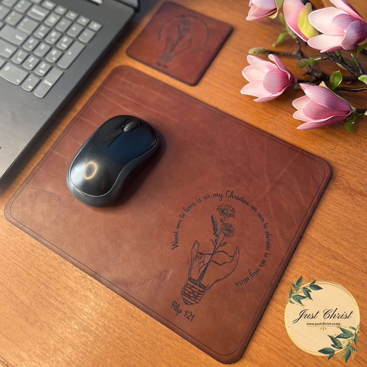 An image of a standard mousepad with a matching coaster which is on a table. A mouse is on the mousepad and there are falsified flowers in the background for decorations.