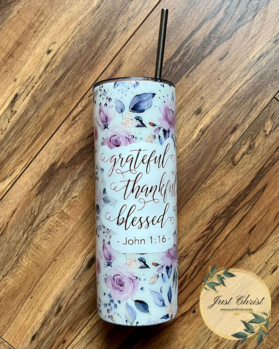 A stainless steel tumbler bottle with its accompanying straw is placed on a wooden floor. The tumbler is decorated with a flower and leaves wrap and the following verse is placed decoratively on it with vinyl: "grateful; thankful; blessed; John 1:16"