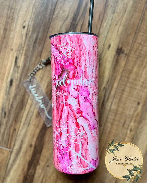 A tumbler bottle with a stainless steel straw in it, as well as a name tag is laying on a wooden floor. The tumbler is pink with a wave effect, and white "Forget me Not" Flowers are on the tumbler by means of vinyl. 