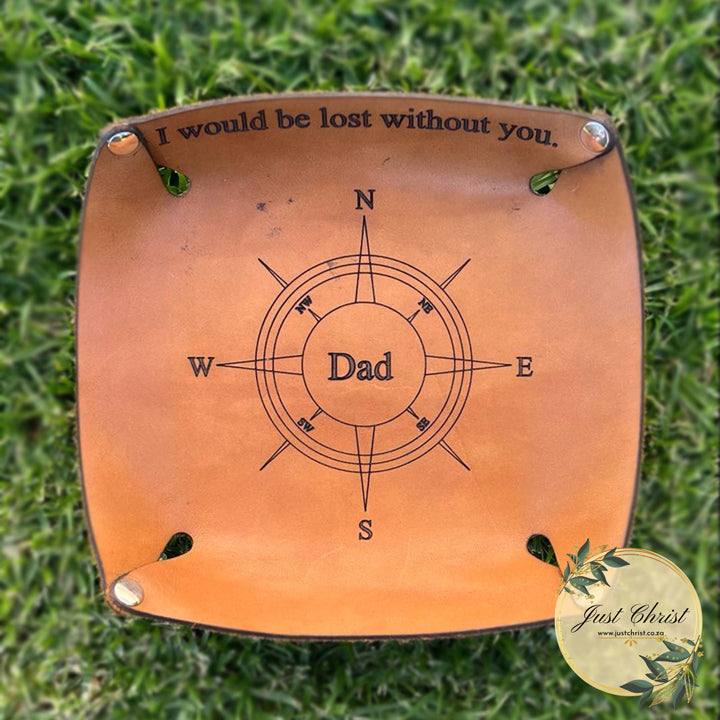 A top view of the leather tray, engraved with a compass with "Dad" in the centre and "I would be lost without you" on the side. The valet tray is on grass.