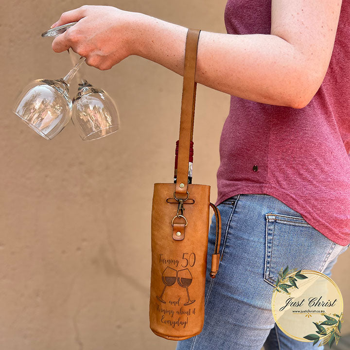 A person is holding two glasses in one hand and the wine carrier is hanging from the forearm. 