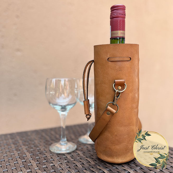 A wine carrier with a wine bottle in it is on a table with two glasses in the background. 